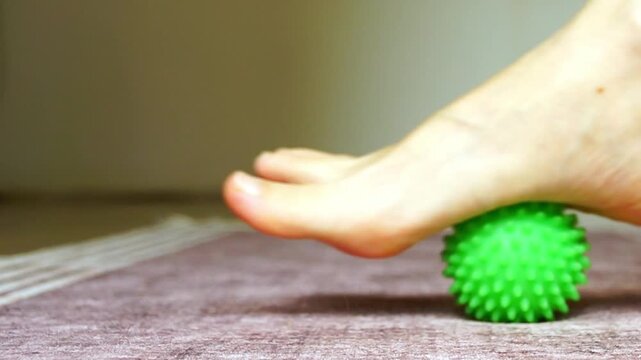 Close view of female foot massaging arch and heel using spiky ball with steady rolling movement in natural light.  Expresses targeted plantar zones, structural support, and functional self-therapy.