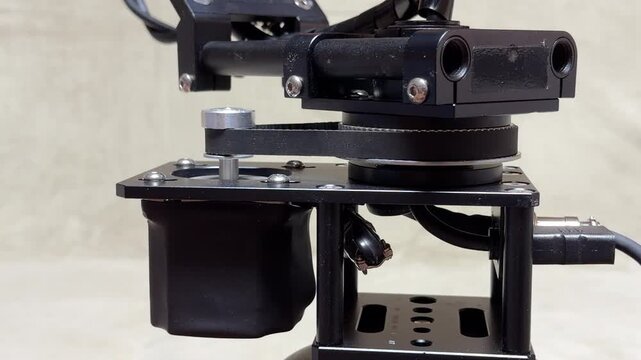 A motorized camera gimbal uses a belt-driven system to rotate its axis. The high-speed motor generates a sharp, mechanical whining sound and a rhythmic whirring during the movement.