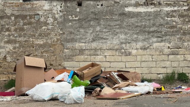 Discarded boxes and white sacks clutter the worn pavement. This messy scene creates a feeling of sadness and neglect in the urban alley. It looks lonely and forgotten.