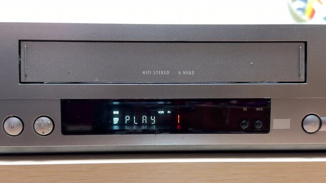 A user inserts a VHS tape into the VCR, triggering the motorized loading mechanism. The device pulls the cassette in with a series of heavy mechanical clunks, followed by a high-pitched whir