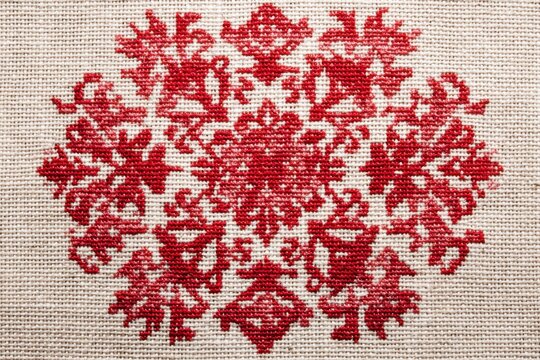 Beige fabric featuring red cross-stitch pattern, detailed embroidery work, traditional needlework design close-up