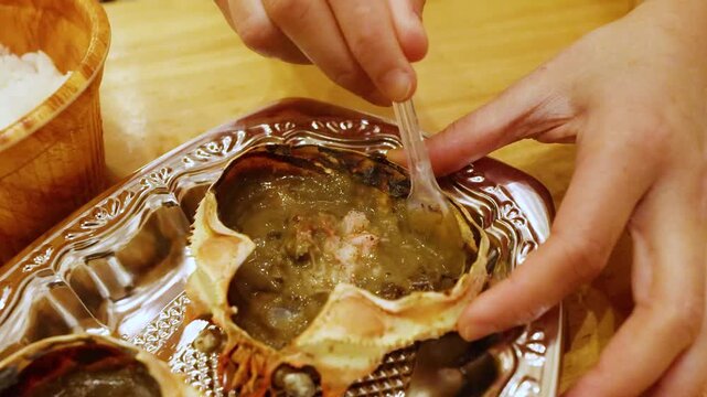 Person mixing traditional japanese kani miso crab brain paste inside shell at restaurant.