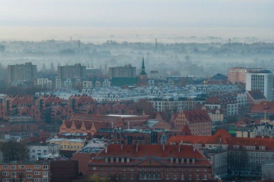Aerial view of the historic old town rooftops with red tiles and a church spire under a misty morning sky in Gdansk, Pomeranian Voivodeship, Poland.