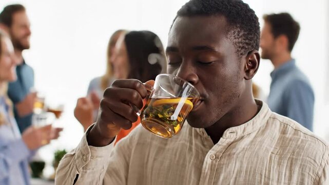 African American man drinking herbal tea at a social gathering. Man enjoying a hot beverage with friends in the background. Healthy lifestyle and social interaction