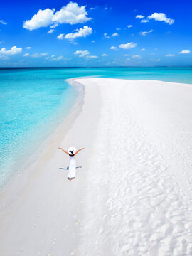 Aerial view of a happy woman in a white dess walking on a beautiful beach with turqouise sea and fine sand in the Maldives islands