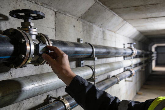 Technician calibrating a flow meter on a large industrial pipe in a concrete tunnel