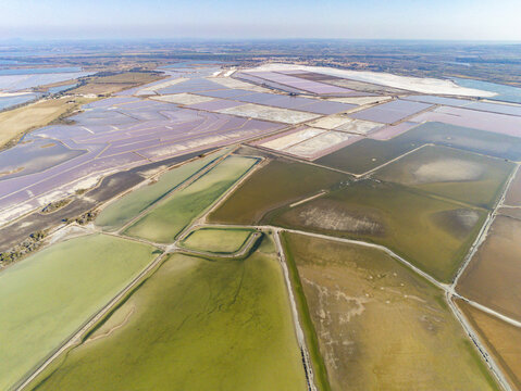 Aerial view of Salin d'Aigues-Mortes featuring colorful salt evaporation ponds and geometric dikes under a clear sky in Aigues-Mortes, Occitanie, France.