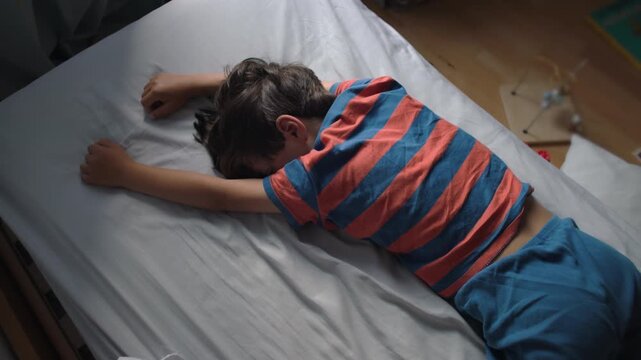Young boy lying face down on bed with arms stretched forward avoiding waking up showing tiredness low energy and reluctance during morning routine at home