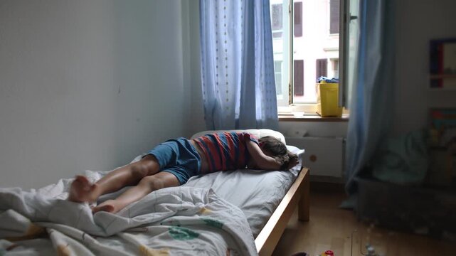 Young boy lying stretched across bed in wide view avoiding getting up showing morning fatigue reluctance and low motivation during quiet home routine