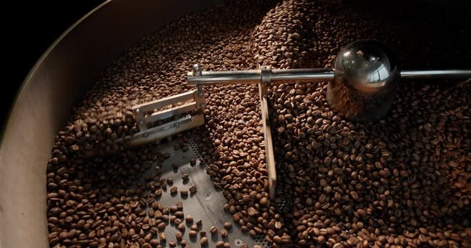 Slow motion roasted coffee beans tumbling inside industrial roaster drum at roastery processing bay..