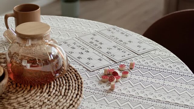 Close up shot of brewed black tea in teapot, cup and traditional lotto board game set on decorative patterned tablecloth in cozy apartment