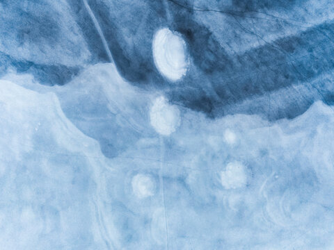 Aerial view of the frozen Lac de Charpal featuring intricate ice patterns and white circular formations on the blue surface in Lozere, Occitanie, France.