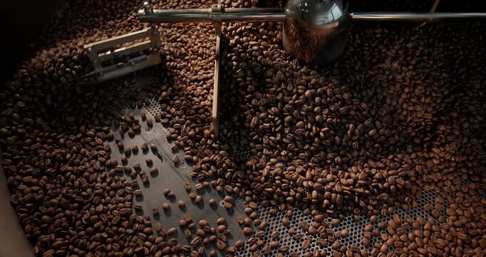 Top view Slow motion coffee beans tumbling inside industrial roaster drum in roastery during cooling process.