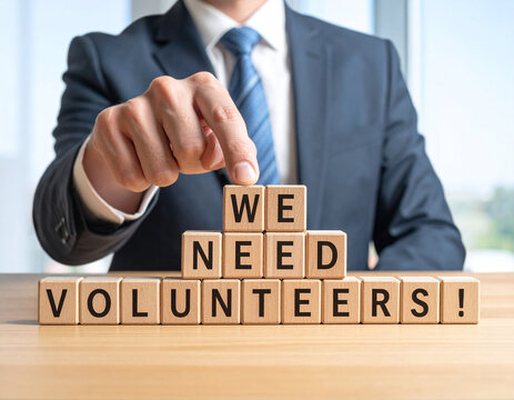 We need Volunteers! - Geschäftsmann zeigt auf das Wort "We need Volunteers!"