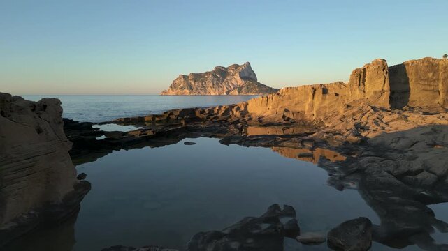 Aerial view flying over rocky coastline toward pe&ntilde;on de ifach at sunrise