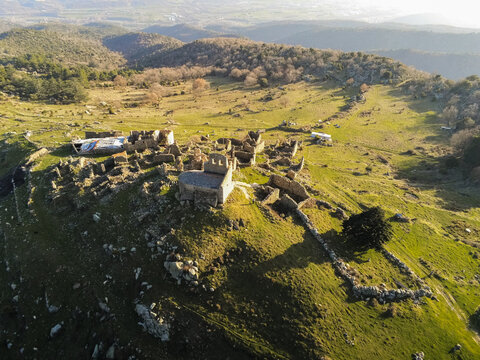 Aerial view of the ancient stone ruins of the abandoned village of Comes on a grassy hilltop in Eus, Occitanie, France.