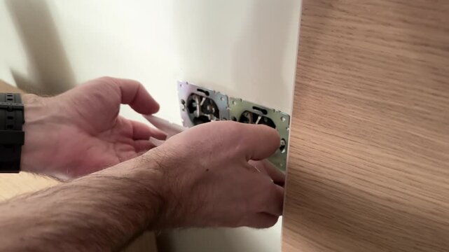 Close-up of a man's hands removing an electrical outlet frame from the wall. Electrician's work at home and electrical safety