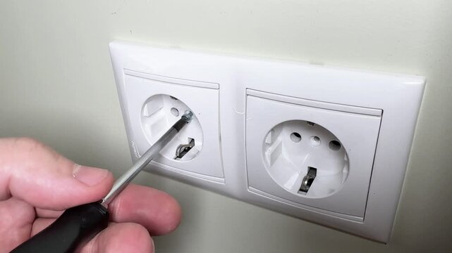 Close-up of a man's hands screwing an electrical outlet to the wall with a screwdriver. Electrician's work and electrical safety