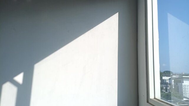 Sunlight casting geometric shadows on a white wall near a window.