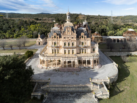 Aerial view of the ornate Chateau d'Aubiry with its grand facade and central tower surrounded by lush green hills and forests in Ceret, Occitanie, France.