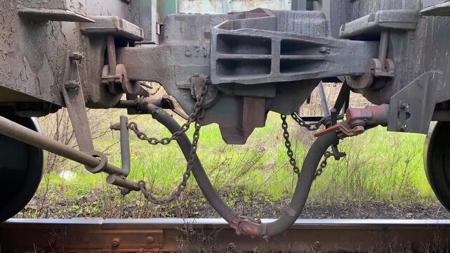 Close-up of a railway automatic coupler connecting two freight cars. Static shot with the chain moving slightly in the wind. Concept of railway transport, logistics and industrial infrastructure. 4K