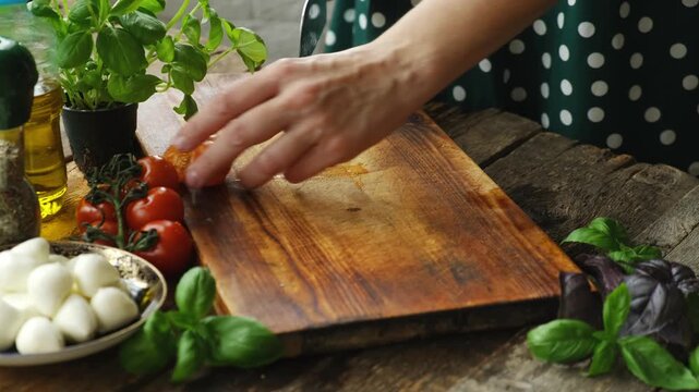 Woman cooking caprese salad. Hands cutting fresh tomatoes on wooden cutting board. Italian cuisine. 