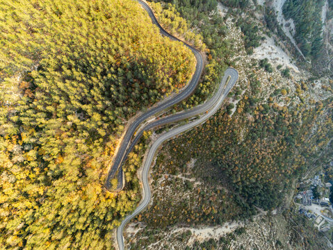 Aerial view of a winding mountain road with sharp hairpin turns through a dense forest near Gorges du Tarn in Saint-Pierre-des-Tripiers, Occitanie, France.