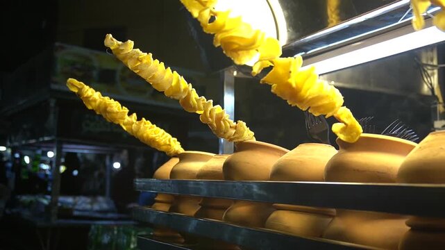 Spiral potato skewers glowing under warm lights at night stall, street snack concept