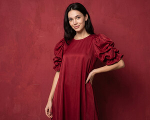Fototapeta premium Young beautiful slender woman in a fashionable red dress with lush sleeves. Woman posing on a red background