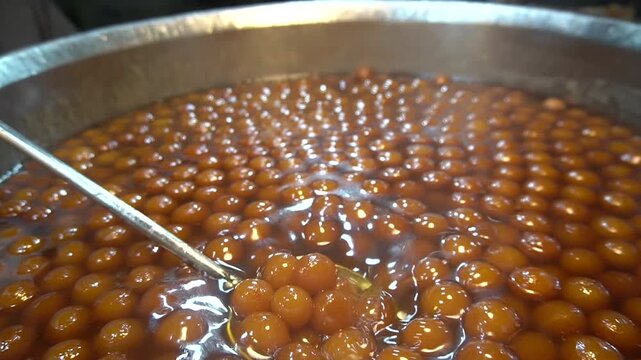 Gulab jamun scooped from syrup, glossy sweet balls close-up, dessert serving concept