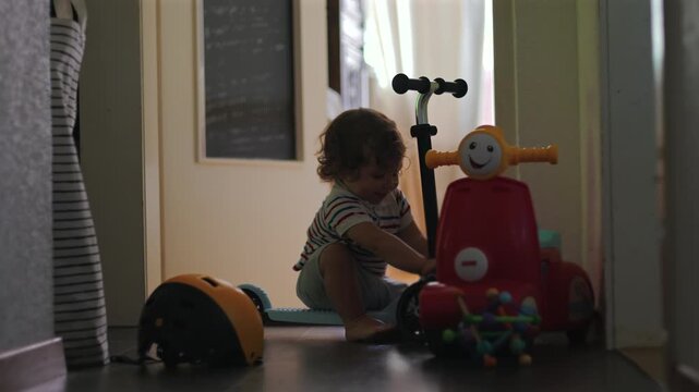 Toddler playing with scooter in hallway exploring toys and learning balance while sitting and reaching creating curious independent moment of early childhood development at home