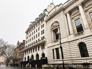 Naklejka premium Historic neoclassical government building facade in London, UK with pedestrians and umbrellas on rainy street