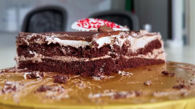 Close-up of a chocolate layer cake slice with cream frosting, caramel glaze, and crumbs on a serving board in a softly lit indoor setting.