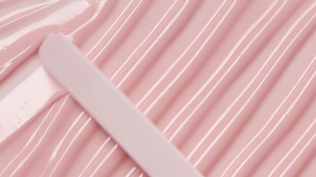 Close up of white spatula smear pink lip gloss texture, satisfying texture stroke. Cosmetic product swatch background	