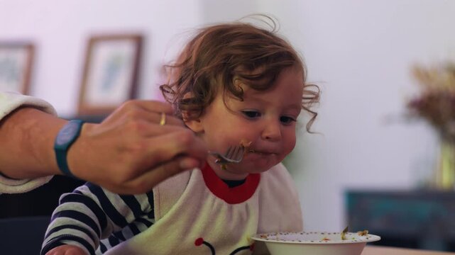 Toddler refusing food while parent offers spoon during mealtime, expressive moment showing feeding difficulty, independence, frustration, and real parenting challenge in everyday family routine