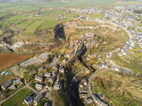 Aerial view of Le trou de Bozouls canyon with historic stone houses and a church perched on the limestone cliffs under bright sunlight Bozouls, Occitanie, France.
