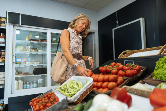 Woman shopping for fresh organic tomatoes in grocery store