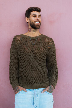Smiling bearded man with tattoos leaning on pink wall