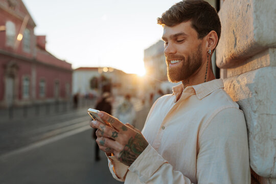 Smiling man using smartphone leaning on wall