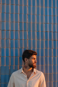 Bearded man smiling against blue tiled wall enjoying golden hour