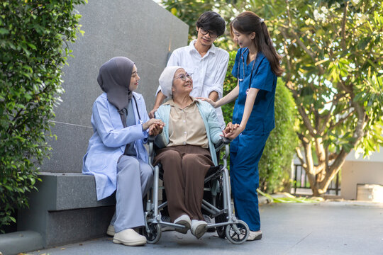 Cancer, Diverse medical team and family supporting senior asian woman cancer patient in wheelchair , Muslim female doctor and nurse holding hand with elderly mother, Chemotherapy, Healthcare caregiver