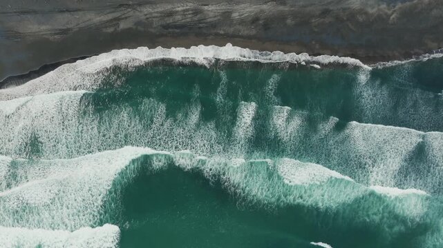Aerial view of powerful waves crashing onto a black sand beach Marokopa, Waikato, New Zealand. The raw beauty of nature's force is on full display.