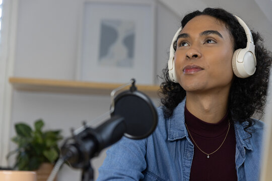 Nonbinary adult wearing white headphones, denim shirt, recording in home studio with mic pop filter