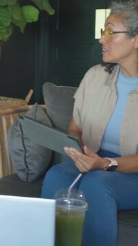 Vertical video: Answering host in yellow specs on sofa holding tablet as guest entering with mic