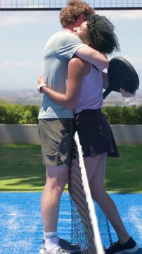 Vertical video: Running man reaching net hugging woman in purple polo on rooftop court with paddles