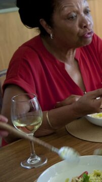 Vertical video: Serving spoon scooping pasta while mom and daughter sharing pasta at home, red top