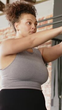 Vertical video: Exhaling adult woman swinging 5kg kettlebell for strength training at gym, gray top