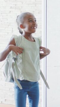Vertical video: Entering child adjusting backpack straps in green top at home, parent guiding