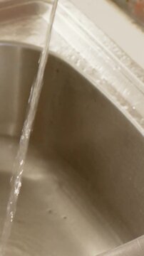 Vertical video: Tap on, hands rinsing and scrubbing carrot at sink, cuff, white watch for cooking