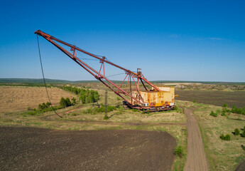 Fototapeta premium Massive industrial dragline excavator rests in an open field, surrounded by sparse vegetation and dirt roads